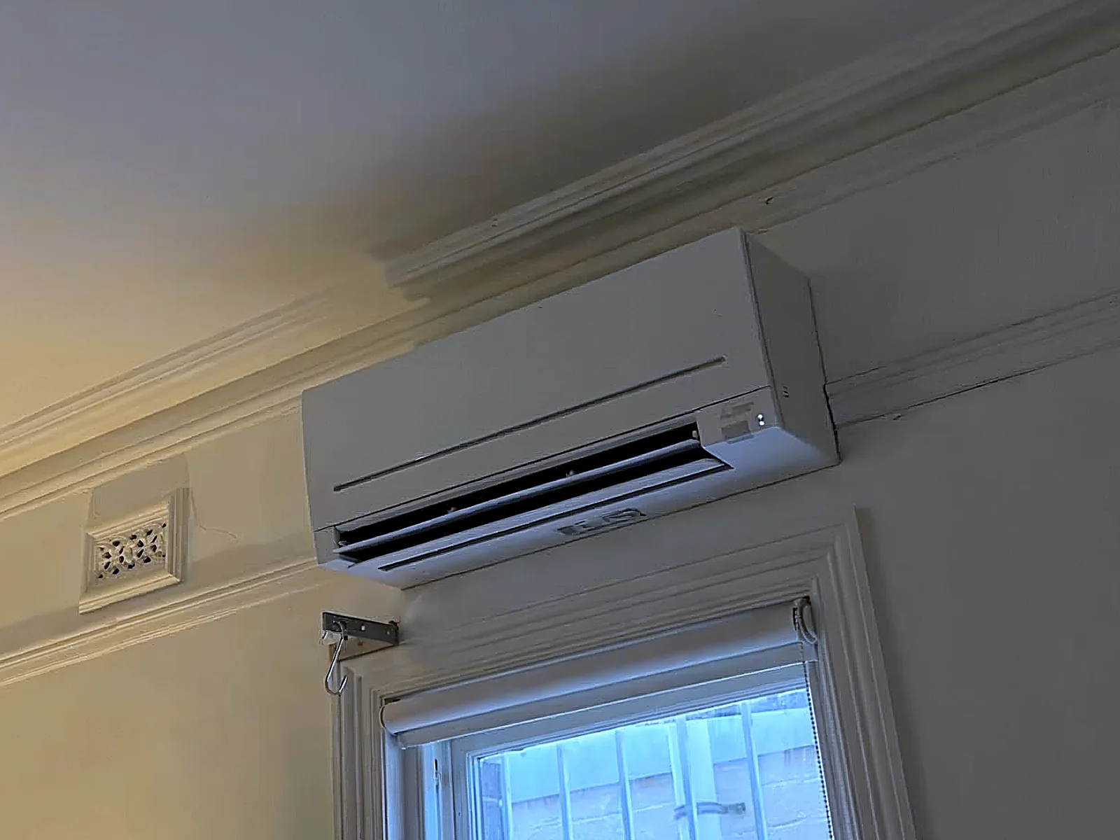Wall-hung split system air conditioning installation above a window in an older Sydney home